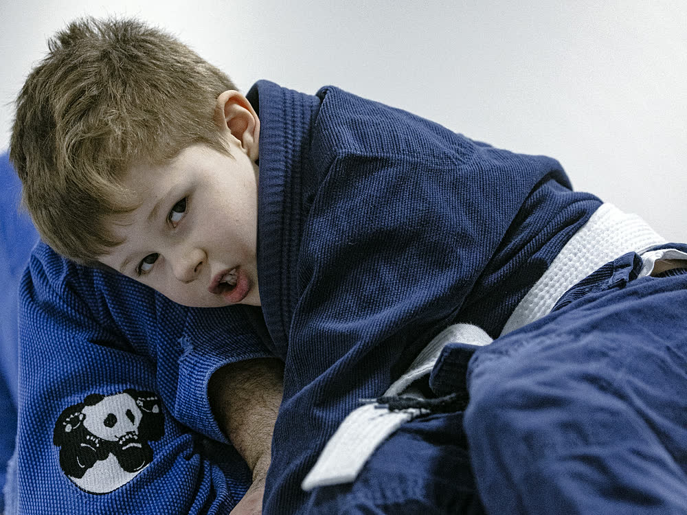 Gutt i blå kimono med pandamerke ser mot kamera under barnetreningen.