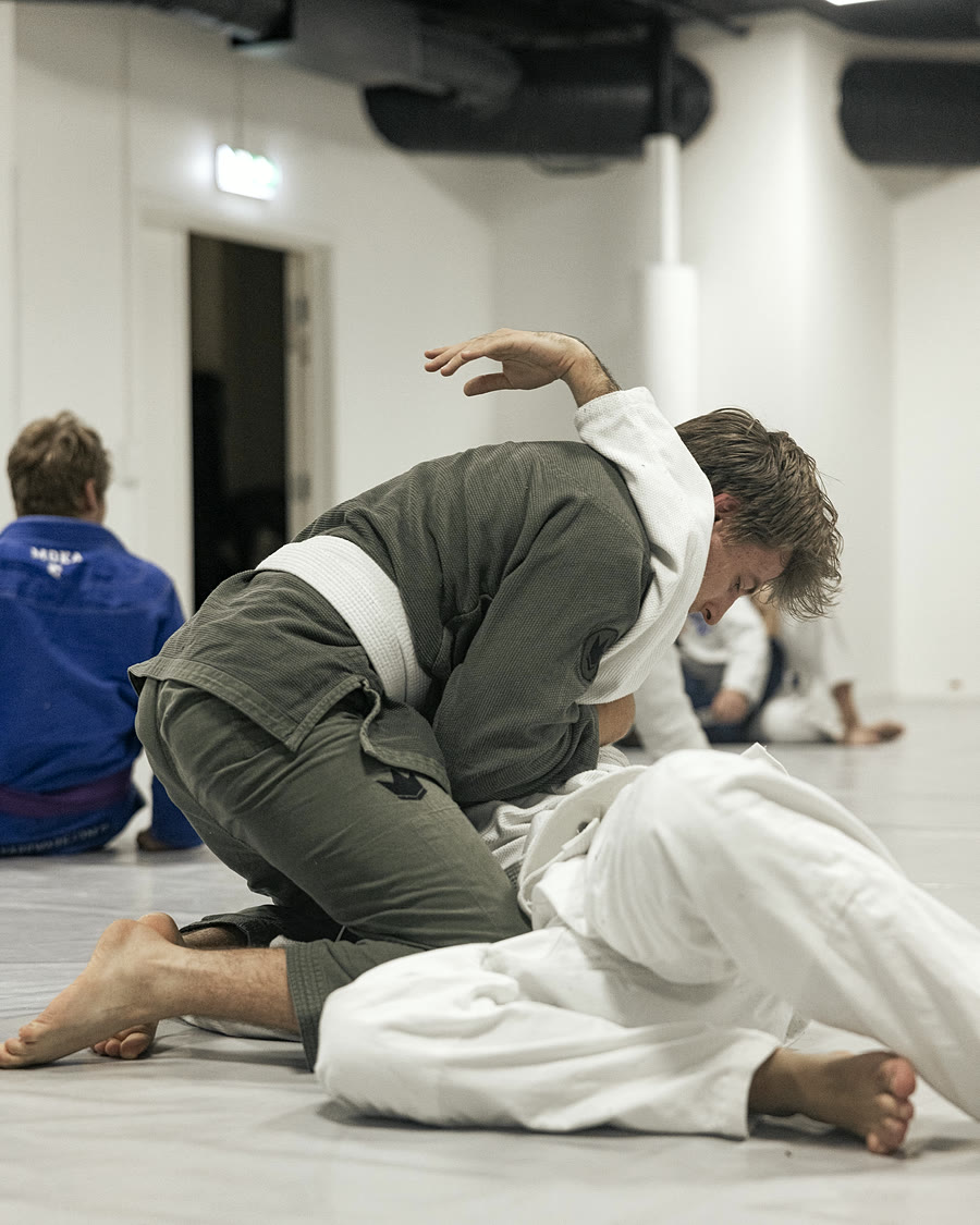 En utøver i blå kimono strekker ut armen midt i en øvelse, under taklysene i klubbens sal i Torggata 83.